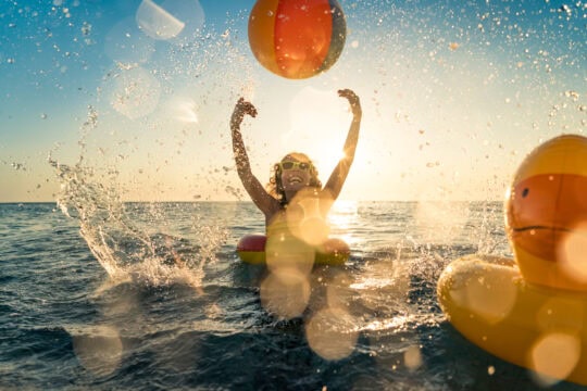 child in water playing with beach ball