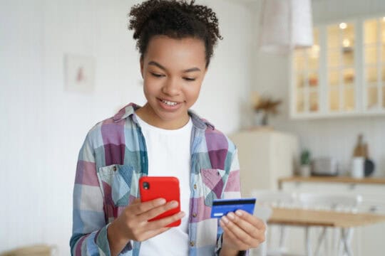 smiling teenager online shopping with a phone and credit card