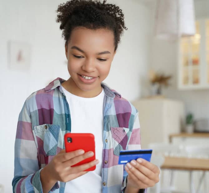 smiling teenager online shopping with a phone and credit card