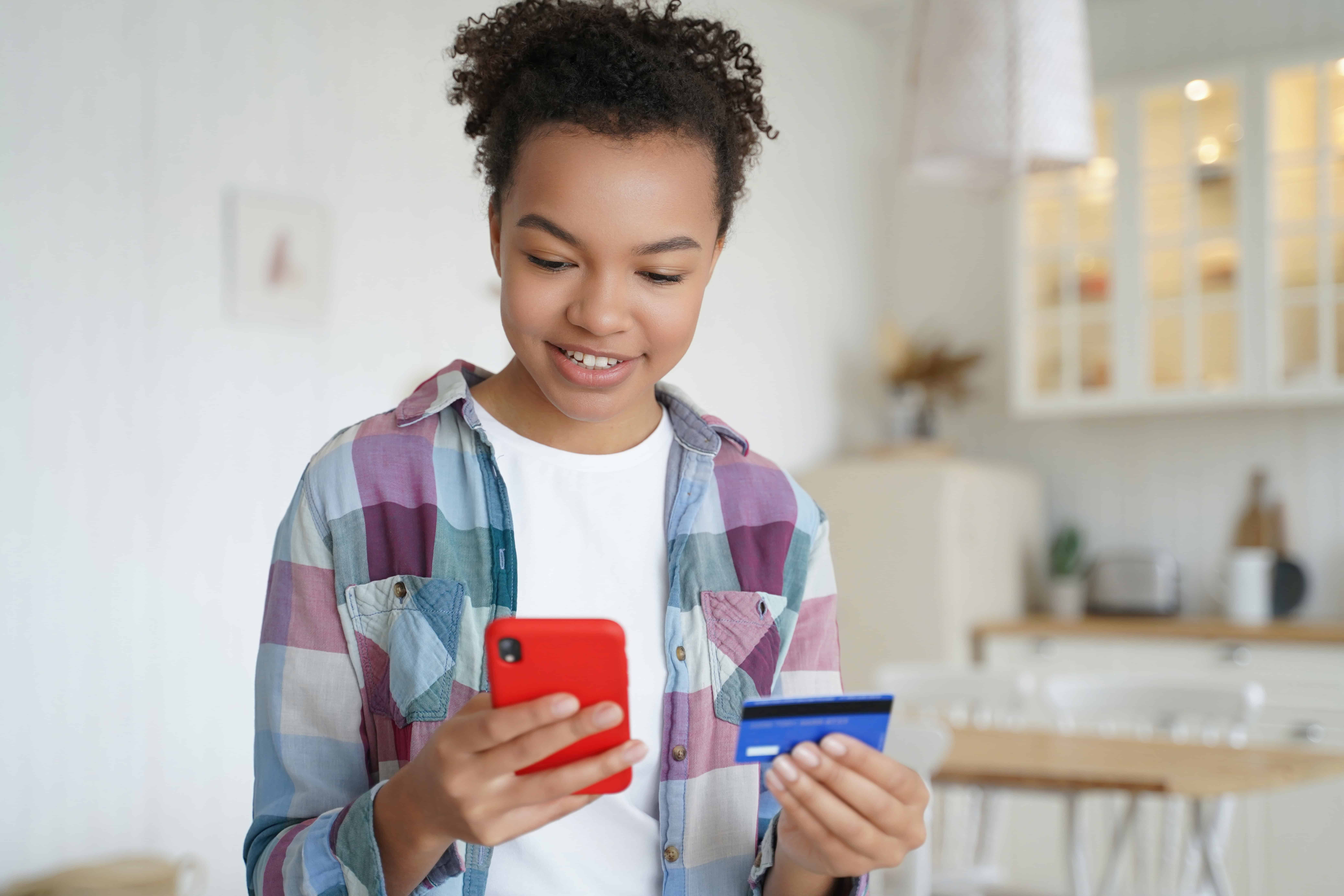 smiling teenager online shopping with a phone and credit card