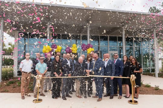People in front of a credit union branch, cutting a ribbon and confetti in the air