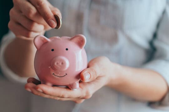 person holding piggy bank and adding coin